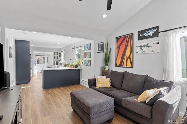 living room with light hardwood / wood-style flooring, baseboard heating, sink, vaulted ceiling, and ceiling fan