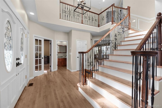 foyer entrance featuring hardwood / wood-style floors, a towering ceiling, and a notable chandelier