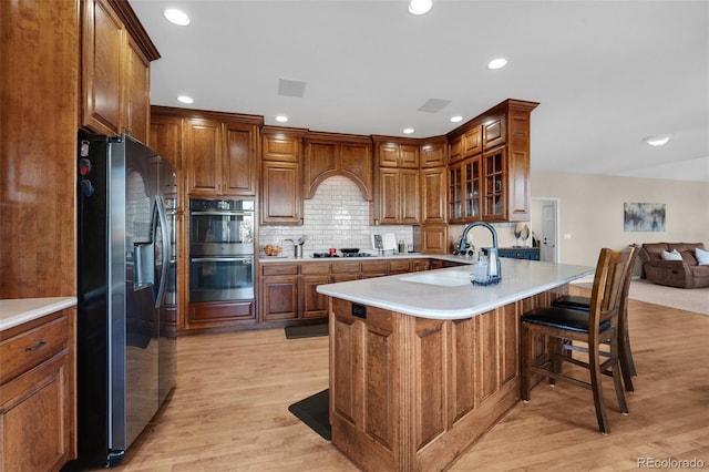 kitchen with decorative backsplash, light wood-type flooring, stainless steel appliances, and a kitchen bar