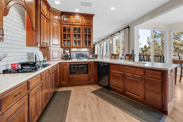 kitchen featuring black appliances, sink, backsplash, kitchen peninsula, and light hardwood / wood-style flooring