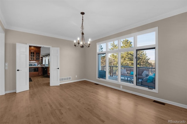 unfurnished dining area featuring hardwood / wood-style flooring, crown molding, and a chandelier