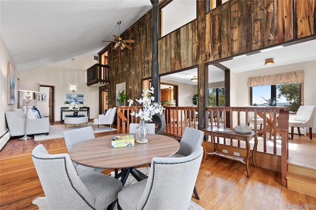 dining room featuring light wood-type flooring, wooden walls, ceiling fan, and high vaulted ceiling