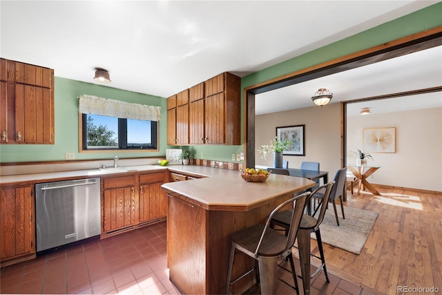 kitchen featuring kitchen peninsula, a breakfast bar area, stainless steel dishwasher, dark hardwood / wood-style floors, and sink