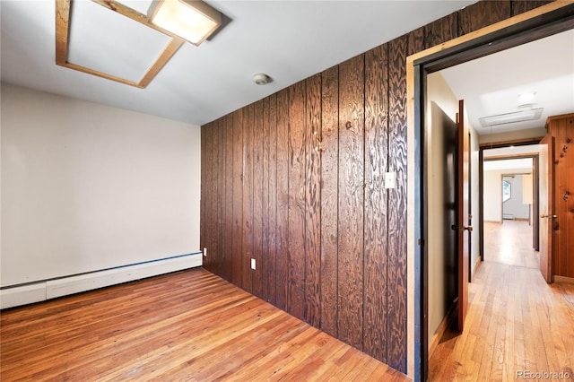 unfurnished room featuring a baseboard radiator, wooden walls, and light hardwood / wood-style flooring