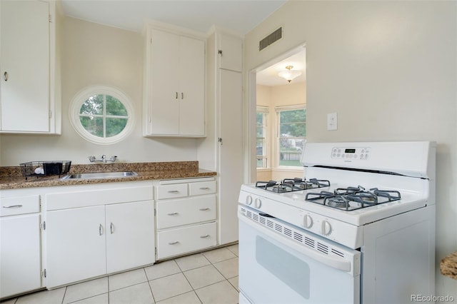 kitchen featuring white gas range oven, white cabinetry, light tile patterned floors, and sink