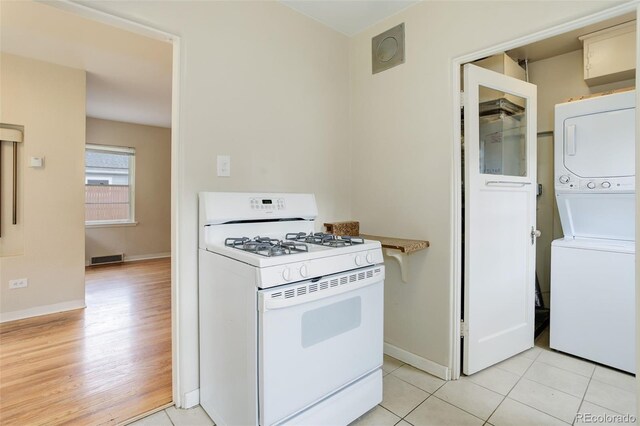 kitchen with stacked washer / drying machine, white gas range oven, and light tile patterned flooring