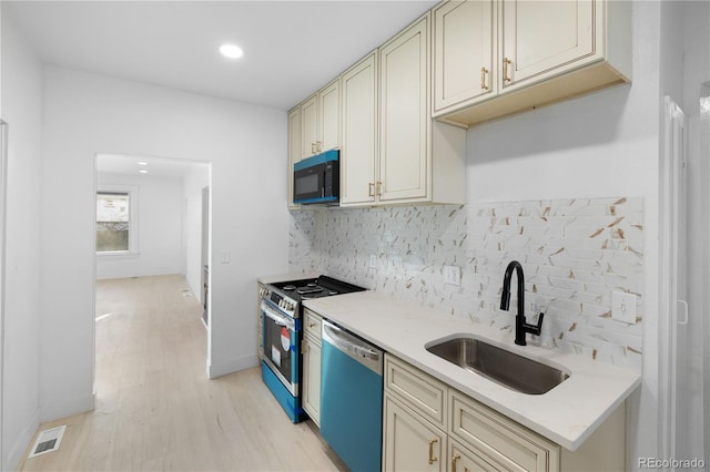 kitchen with backsplash, light stone counters, stainless steel appliances, sink, and cream cabinetry