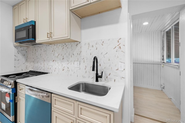 kitchen featuring light stone counters, stainless steel dishwasher, sink, cream cabinets, and range