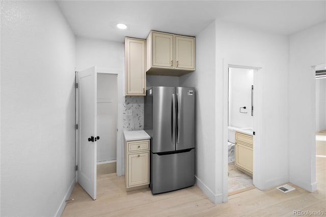 kitchen featuring cream cabinetry, light wood-type flooring, tasteful backsplash, and stainless steel refrigerator