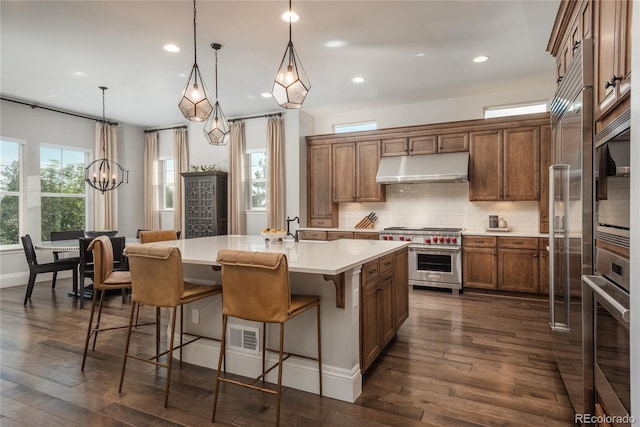 kitchen with pendant lighting, appliances with stainless steel finishes, dark hardwood / wood-style flooring, and a kitchen island with sink