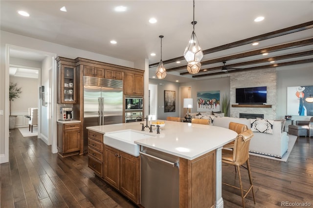 kitchen with dark wood-type flooring, built in appliances, sink, and a center island with sink