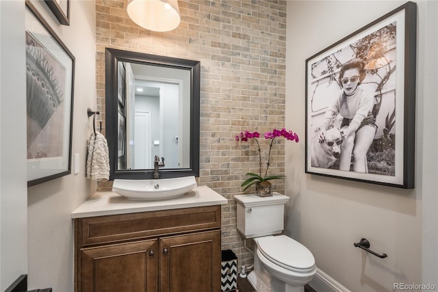 bathroom with brick wall, vanity, and toilet