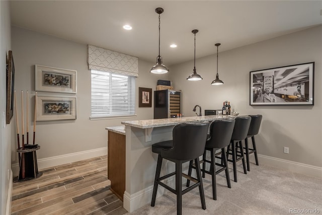 bar featuring light stone countertops, sink, hanging light fixtures, and light wood-type flooring