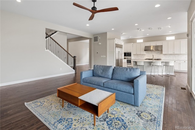 living room with ceiling fan, visible vents, baseboards, dark wood-style floors, and stairs