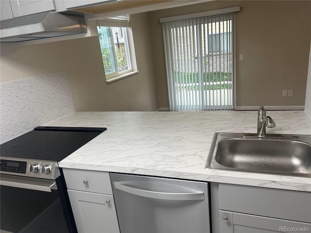 kitchen with appliances with stainless steel finishes, a sink, light countertops, tasteful backsplash, and gray cabinetry