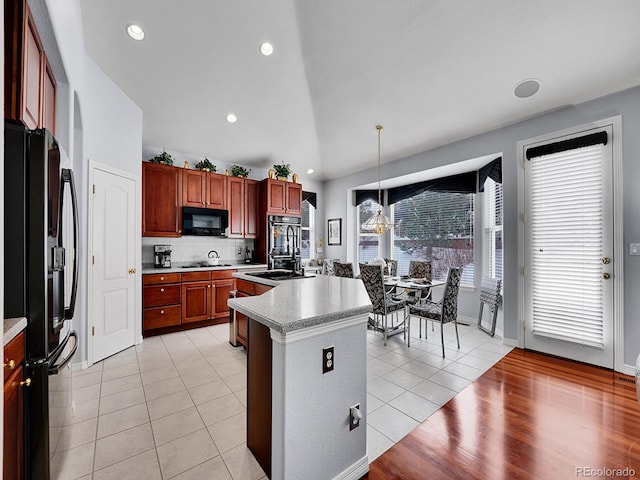 kitchen featuring tasteful backsplash, a kitchen island with sink, black appliances, pendant lighting, and light tile patterned floors