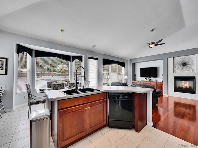 kitchen featuring sink, light tile patterned floors, a center island with sink, black dishwasher, and a tiled fireplace