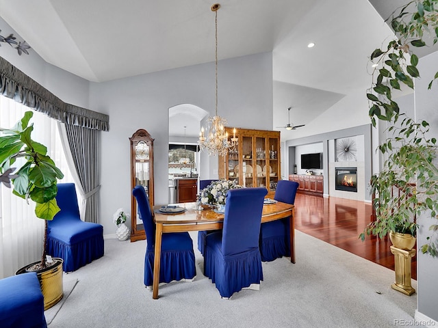 carpeted dining space with a fireplace, high vaulted ceiling, and ceiling fan with notable chandelier