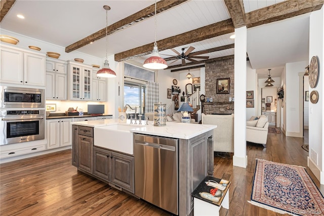 kitchen with appliances with stainless steel finishes, white cabinets, hanging light fixtures, a kitchen island with sink, and dark wood-type flooring