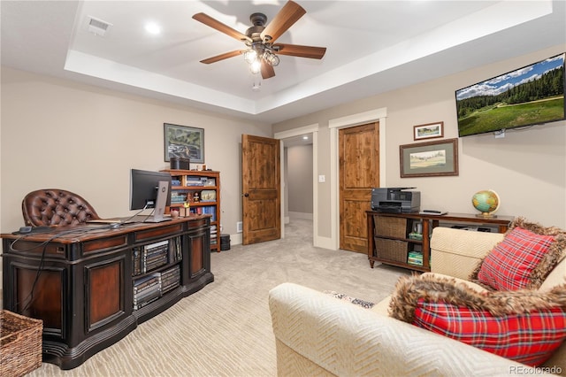 home office featuring light carpet, ceiling fan, and a tray ceiling