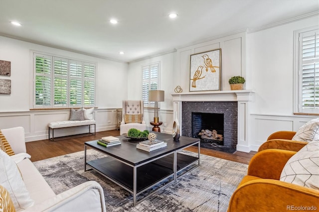 living room with wood-type flooring, a fireplace, a wealth of natural light, and ornamental molding