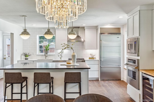 kitchen with beverage cooler, sink, built in appliances, a center island, and hanging light fixtures