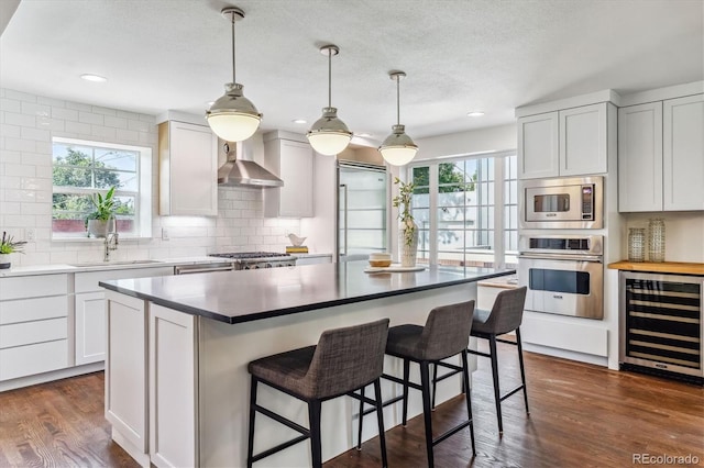 kitchen with white cabinetry, sink, stainless steel appliances, wall chimney range hood, and wine cooler