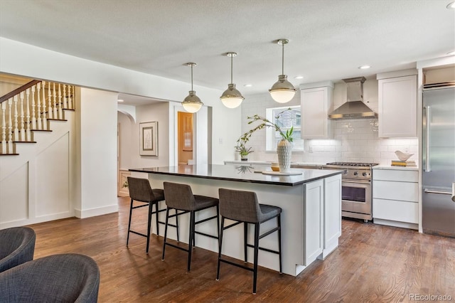 kitchen featuring hanging light fixtures, wall chimney range hood, a kitchen island, high quality appliances, and white cabinets