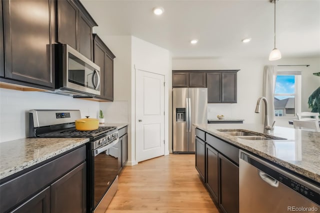 kitchen featuring sink, dark brown cabinets, hanging light fixtures, appliances with stainless steel finishes, and light stone countertops