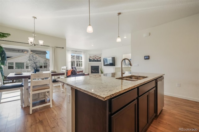 kitchen with sink, dark brown cabinetry, light stone counters, light hardwood / wood-style floors, and stainless steel dishwasher