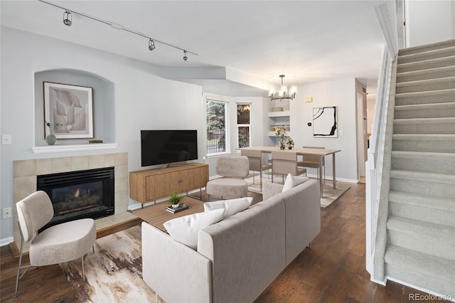 living area featuring stairway, a chandelier, dark wood-type flooring, rail lighting, and a fireplace