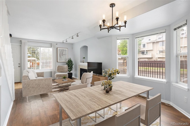 dining area with arched walkways, dark wood finished floors, rail lighting, a chandelier, and healthy amount of natural light