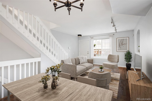 living area featuring rail lighting, wood finished floors, a chandelier, arched walkways, and baseboards