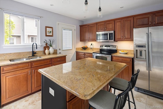 kitchen with stainless steel appliances, a sink, a breakfast bar, light stone countertops, and a center island