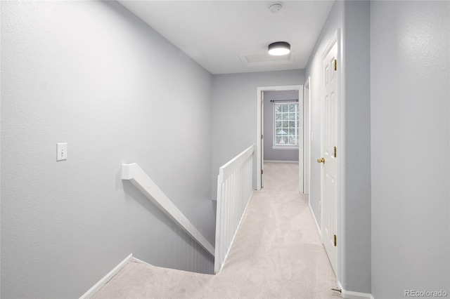 corridor with an upstairs landing, light carpet, attic access, and baseboards