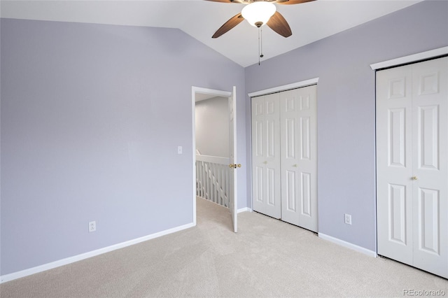 unfurnished bedroom featuring lofted ceiling, light colored carpet, baseboards, two closets, and a ceiling fan