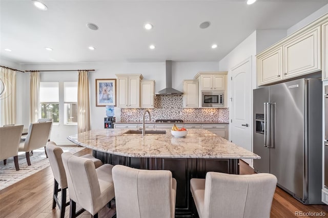 23615 E Del Norte Pl, Aurora, CO 80016 - kitchen featuring appliances with stainless steel finishes, cream cabinetry, wall chimney exhaust hood, light stone countertops, and a kitchen breakfast bar