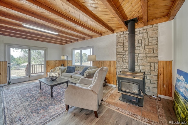 living room featuring beam ceiling, light hardwood / wood-style flooring, wooden ceiling, and a wood stove