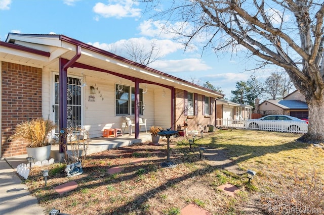 exterior space with covered porch, fence, a front lawn, and brick siding