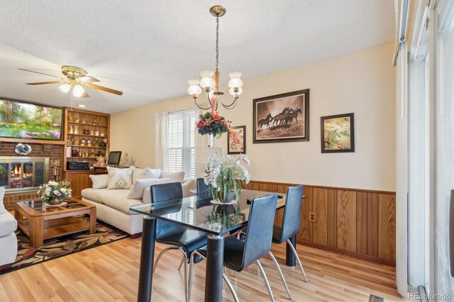 dining room with a textured ceiling, a wainscoted wall, a fireplace, built in features, and light wood-style floors