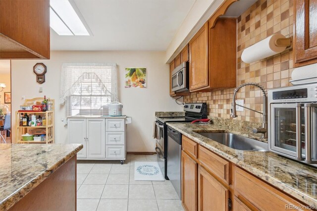 kitchen featuring light stone counters, brown cabinets, light tile patterned floors, appliances with stainless steel finishes, and a sink