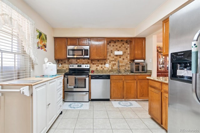 kitchen with appliances with stainless steel finishes, backsplash, a sink, and light tile patterned flooring