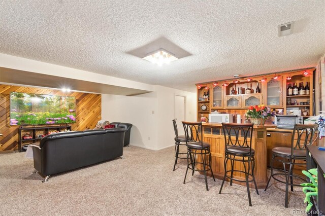 bar with a dry bar, light colored carpet, white microwave, a textured ceiling, and wooden walls