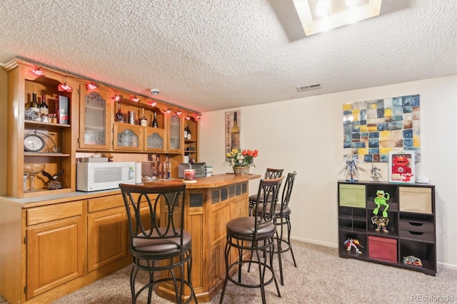 bar with a dry bar, light colored carpet, visible vents, white microwave, and a textured ceiling