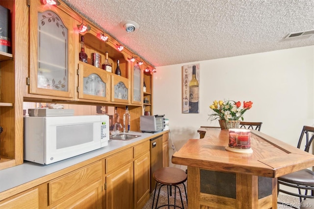 kitchen featuring a textured ceiling, light countertops, white microwave, and a sink