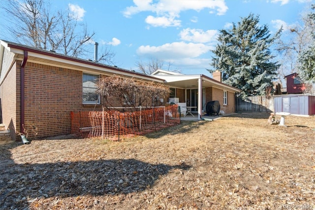 rear view of house featuring a chimney, an outbuilding, fence, a patio area, and brick siding