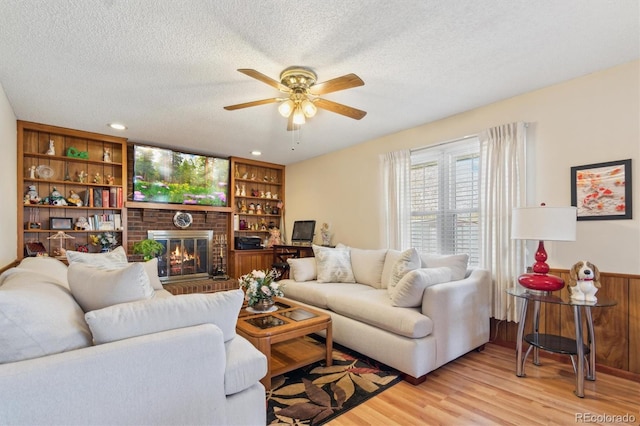 living room with light wood-style flooring, a fireplace, a textured ceiling, and built in shelves