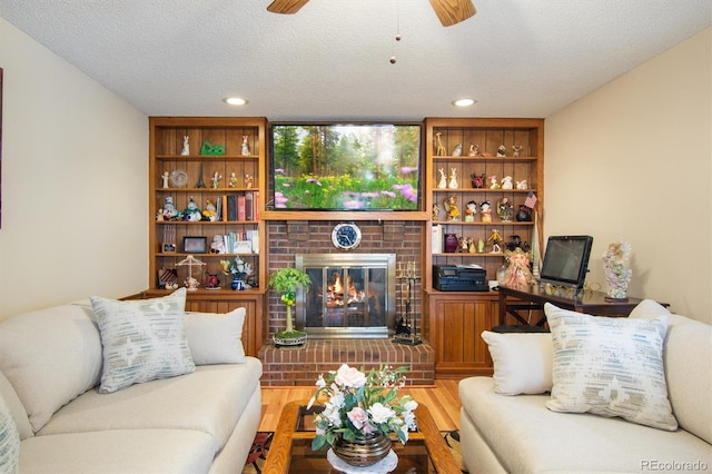 living room with ceiling fan, a fireplace, a textured ceiling, and wood finished floors