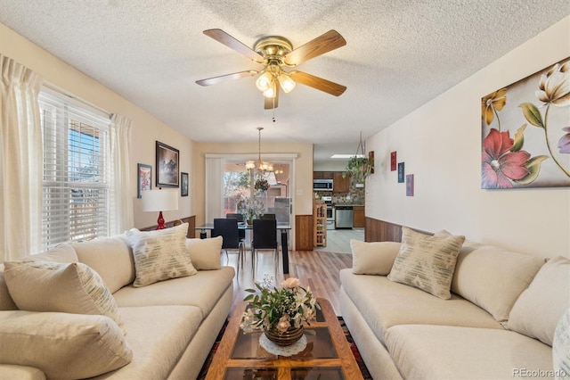 living area featuring light wood-style floors, plenty of natural light, a textured ceiling, and ceiling fan with notable chandelier