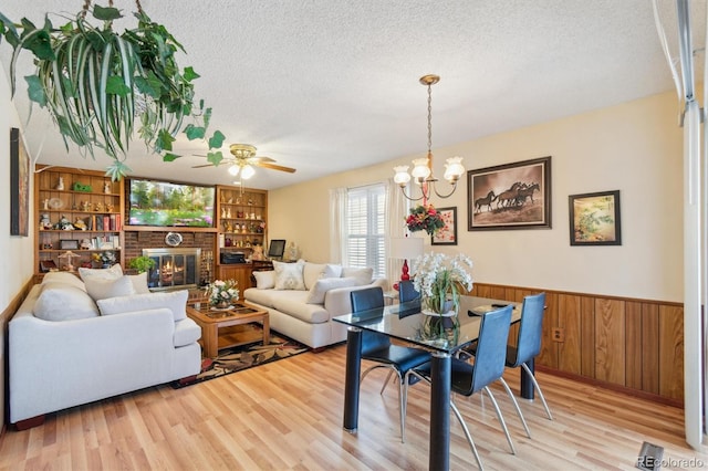 interior space with wainscoting, light wood-style flooring, a textured ceiling, wood walls, and a brick fireplace